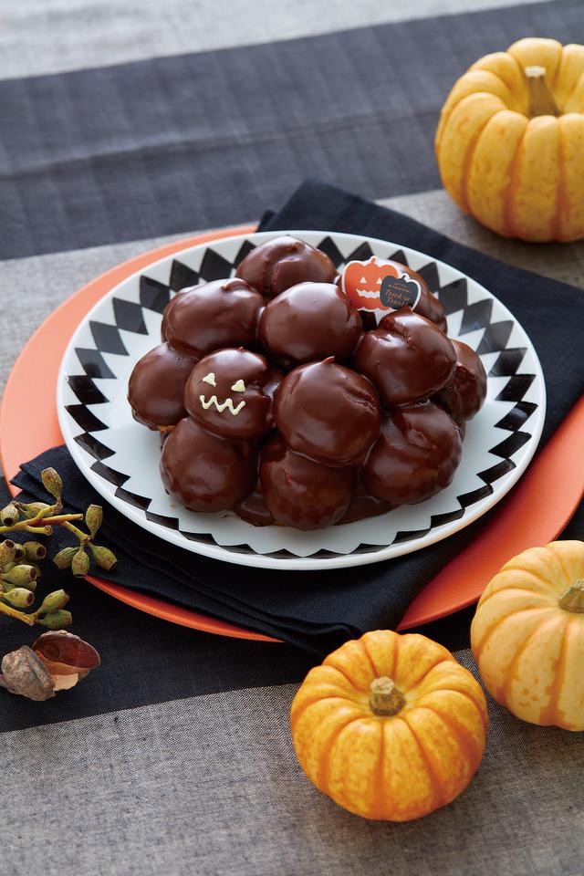 画像: <商品概要> NEW ■商品名:ハロウィン プロフィットロール ■価格:1,620円(税込) ■販売期間:10月15日(土)、16日(日)、21日(金)~31日(月) ※10月1日(土)から予約受付開始 ■商品説明:やさしい甘さのミルクチョコクリームをつめたプチシューを積み上げたプロフィットロール※に、口どけのよいチョコレートでコーティング。ミルクチョコレートを練りこんだザクサク食感のクッキーの土台がアクセント。コーティングのチョコレートにはオリーブオイルを使って軽さを出しました。 ※プロフィットロール・・ひとくちサイズの小さなシュークリームを積み上げたもの