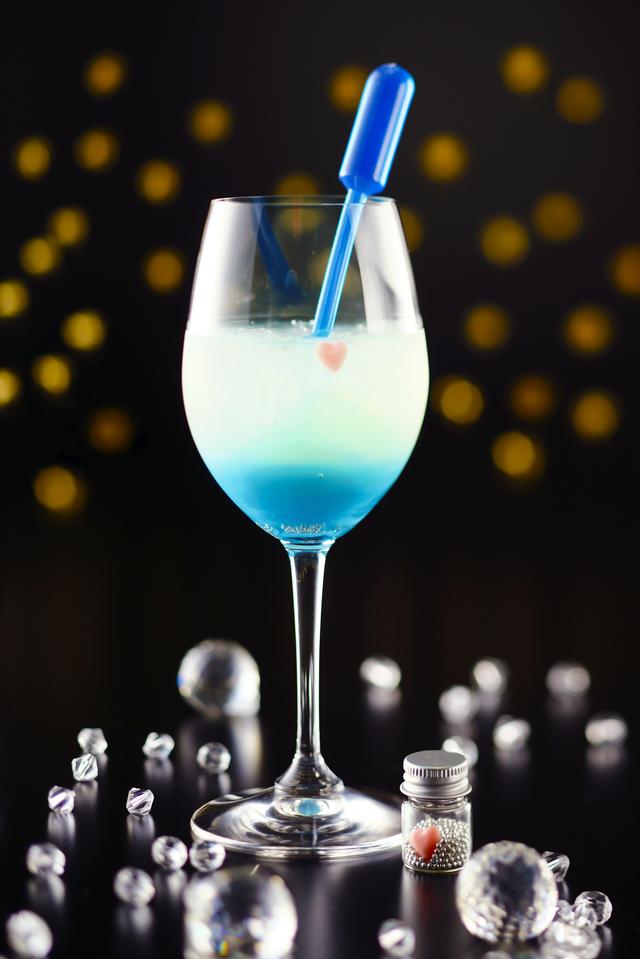画像: 【5・6月限定】スピカ 春の大三角のひとつである、おとめ座の1等星「スピカ」。別名「真珠星」とも呼ばれる青白く輝くスピカを、白ワインベースのカクテルに、スポイトにはいったブルーシロップをゆっくり絞ると完成する、美しい2層のカクテルで表現。小瓶の中の、真珠に見立てたアラザンシュガーとハートのチョコレートを添えて。