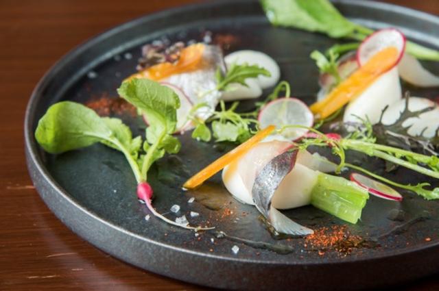 画像: 大分「関あじ」と青森「野辺地小かぶ」の冷菜 1,800 円(税込) 大好きなこの大分・佐賀関漁港へはもう2度見学に伺いました。この有名な「関アジ」は、潮流が速い豊予海峡を越えることによって身が引き締まり非常に脂がのっているのが特徴です。また、熟練の漁師が一本釣りしたものを一旦いけすで魚を休ませたあと出荷します。その際、鮮度を保つために漁港で活け締めをして各地へ発送されます。そして、もう一つの主役「野辺地小かぶ」は夏でも冷涼な土地で毎日夜明け前に採られ市場に送られます。鮮度の良いこの「小かぶ」は非常にみずみずしく生でも食べられ、その皮は手でも簡単に剥けるほどです。さっぱりとしたホワイトバルサミコビネガーをアクセントにしたこの時期ならではの前菜に仕上げました。