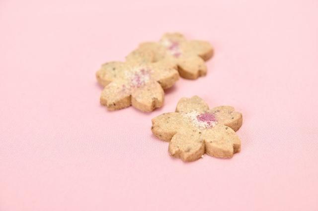 画像: 『桜のショートブレッド』 塩漬けの桜の葉を加えた、少し塩味のある生地のショートブレッドです。アクセントに桜の花びらのフレークとパルメザンチーズをふって仕上げました。一口食べるとふわっと広がるバターの優しいコクに、塩漬けの桜の葉のほのかな塩味が口いっぱいに広がって春らしい味わいが楽しめます。桜の花の形と濃いピンクの桜の花びらフレークが、桜の季節にぴったりの毎年春に販売するロングセラー商品です。