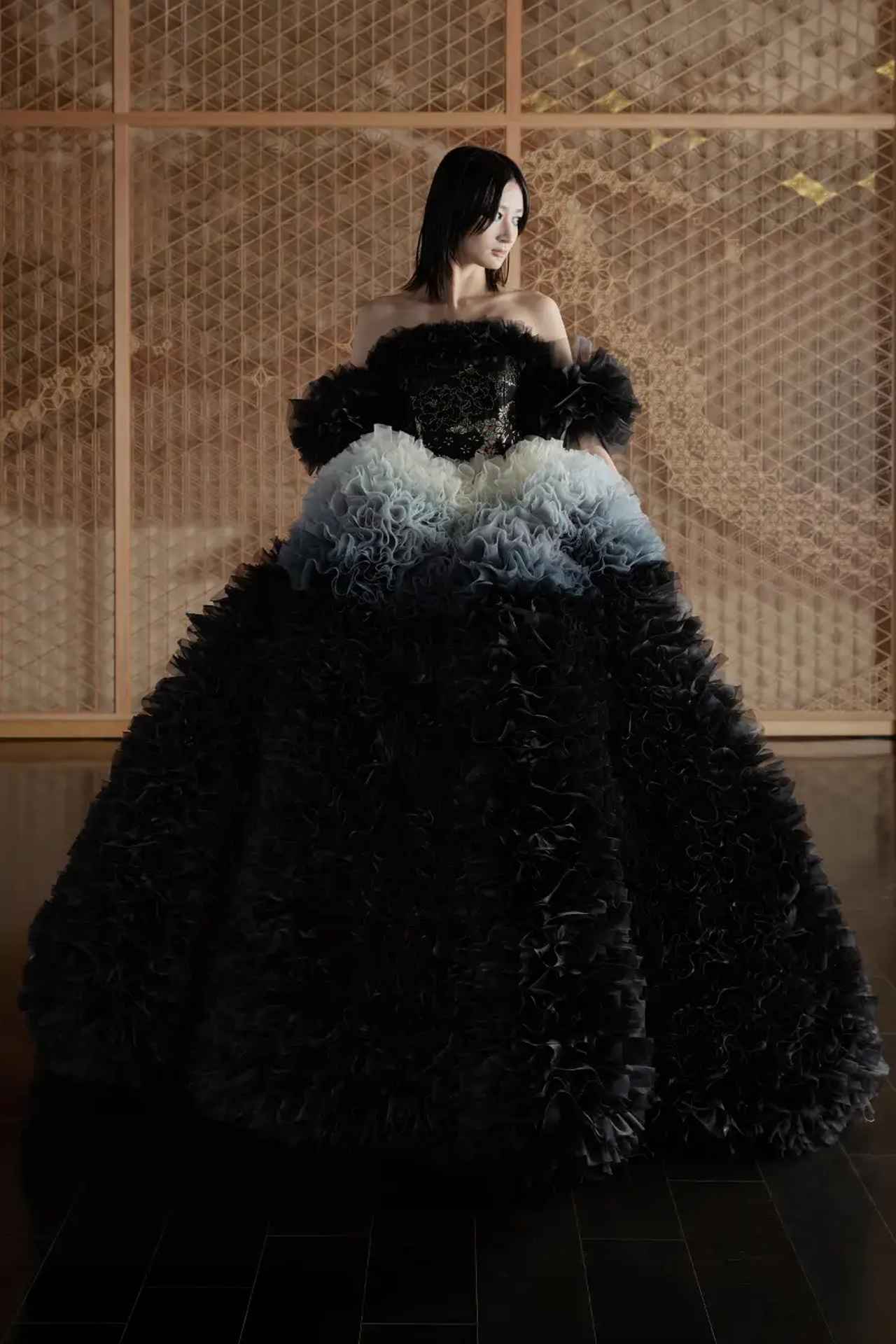 画像: 白から黒へ、滑らかなグラデーションフリルが可憐な「KOKU」。 ウェストから裾元にかけて見事なグラデーションを奏でるフリルは、緻密に計算された構築的なパターンによって、より華やかなオーラを放ちます。 金糸が織り込まれた唐織のビスチェは、重厚感のある佇まいを演出。「KOKU」と「HAKU」どちらも、着物で使用する正絹の経糸を利用し、ビスチェの織り地に仕上げています。 いずれのデザインも、デコルテ、ショルダーのフリルデザインをお好みに合わせて着脱することが可能で、パーソナリティ溢れる装いをお楽しみいただけます。