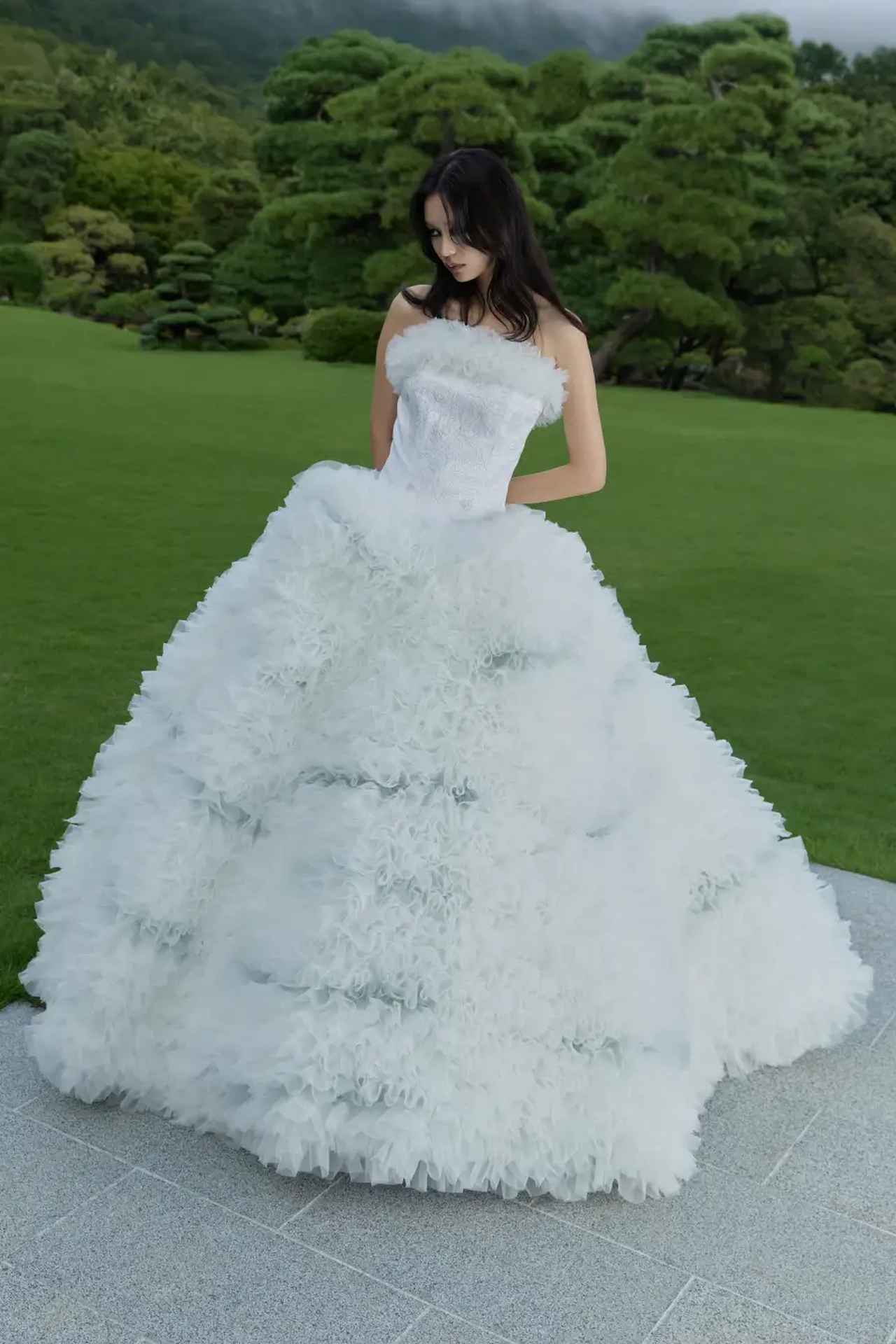 画像: ひときわ目を惹く「TOMO KOIZUMI」を代表するフリルデザインは、ホワイトを基調としながら部分的にグレーの布地を取り入れ、奥行きのある陰影を演出。「KOTOHOGI」にて人気のオリジナルの色打掛と同柄であるビスチェ部分は、京都北部にて「善王寺織（ぜんのうじおり）」で織られた着物の織地を用いており、銀刺繍で施された椿が幻想的な美しさを放ちます。  「KOKU」同様に、いずれのデザインも、デコルテ、ショルダーのフリルデザインをお好みに合わせて着脱することが可能です。