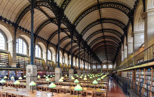 画像: サント=ジュヌヴィエーヴ図書館(1843)の2階閲覧室。平行する2つのヴォールト天井を鋳鉄でつくられたアーチと鉄柱が支える。長辺方向いっぱいに延びた大天井とそれを支える繊細優美な鉄のデザインのコントラストが素晴らしい。設計者のアンリ・ラブルースト(1801-75)は旧国立図書館でも閲覧室をデザインしているが、彼のこのもうひとつの代表作は、ミシェル・フーコーが通い日中こもって作業をしたことでも知られる。