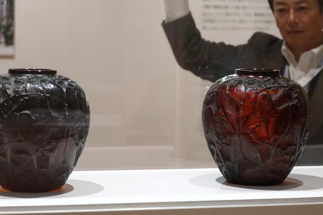 画像: ルネ・ラリック 花瓶「インコ」 一対、1919年 個人蔵 厚手の色ガラスに斜め上から光をあててみると表情が変わるデモンストレーション中。