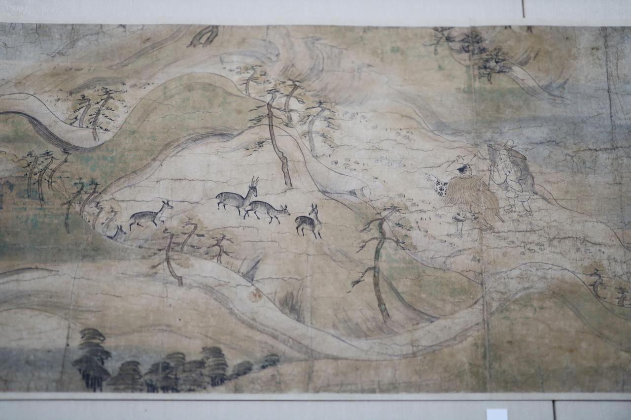 画像: 国宝 信貴山縁起絵巻 尼公巻（部分）平安時代・12世紀 奈良・朝護孫子寺 展示期間：4月19日～5月18日 大仏のお告げを受けて信貴山に向かって旅を続ける尼公。大自然の描写が美しく、丸みを帯びた山々はやまと絵風景画の典型。迎えるの鹿は春日明神の使いの霊獣で、つまりこの大自然はそのまま、仏と神々が宿る神聖な大地なのだ。