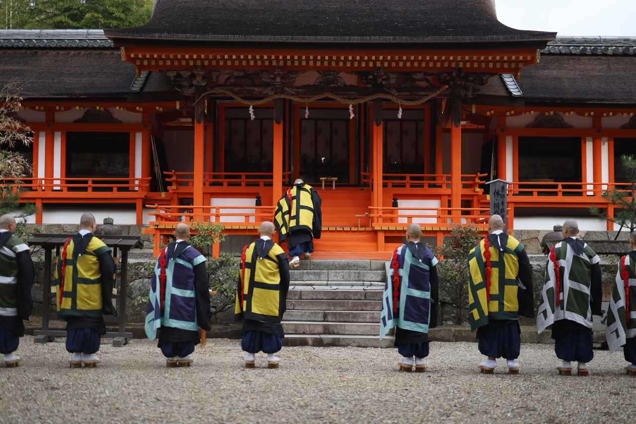 画像: 薬師寺の鎮守・休ヶ岡八幡宮を参拝し法要を行う薬師寺の僧侶。社殿は鎌倉時代で重要文化財。 本展ではここに祀られていた八幡三神坐像（国宝）と吉祥天像（国宝）、この写真では左右の回廊の中に見える板絵神像（重要文化財）、狛犬、古神宝を並べて展示し、かつての礼拝空間を再現している。