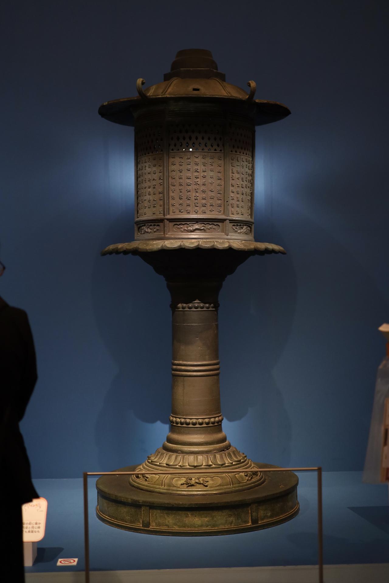 画像: 国宝 金銅燈籠 平安時代・弘仁7年（816) 奈良・興福寺 非常に細かな展示の工夫だが、照明で燈籠の灯を納める部分が光を放っているかのように見せている。 なお「尼公巻」で大仏の正面に描かれている、東大寺の金銅の八角燈籠（国宝・奈良時代）の扉は、後期5月20日以降展示される。
