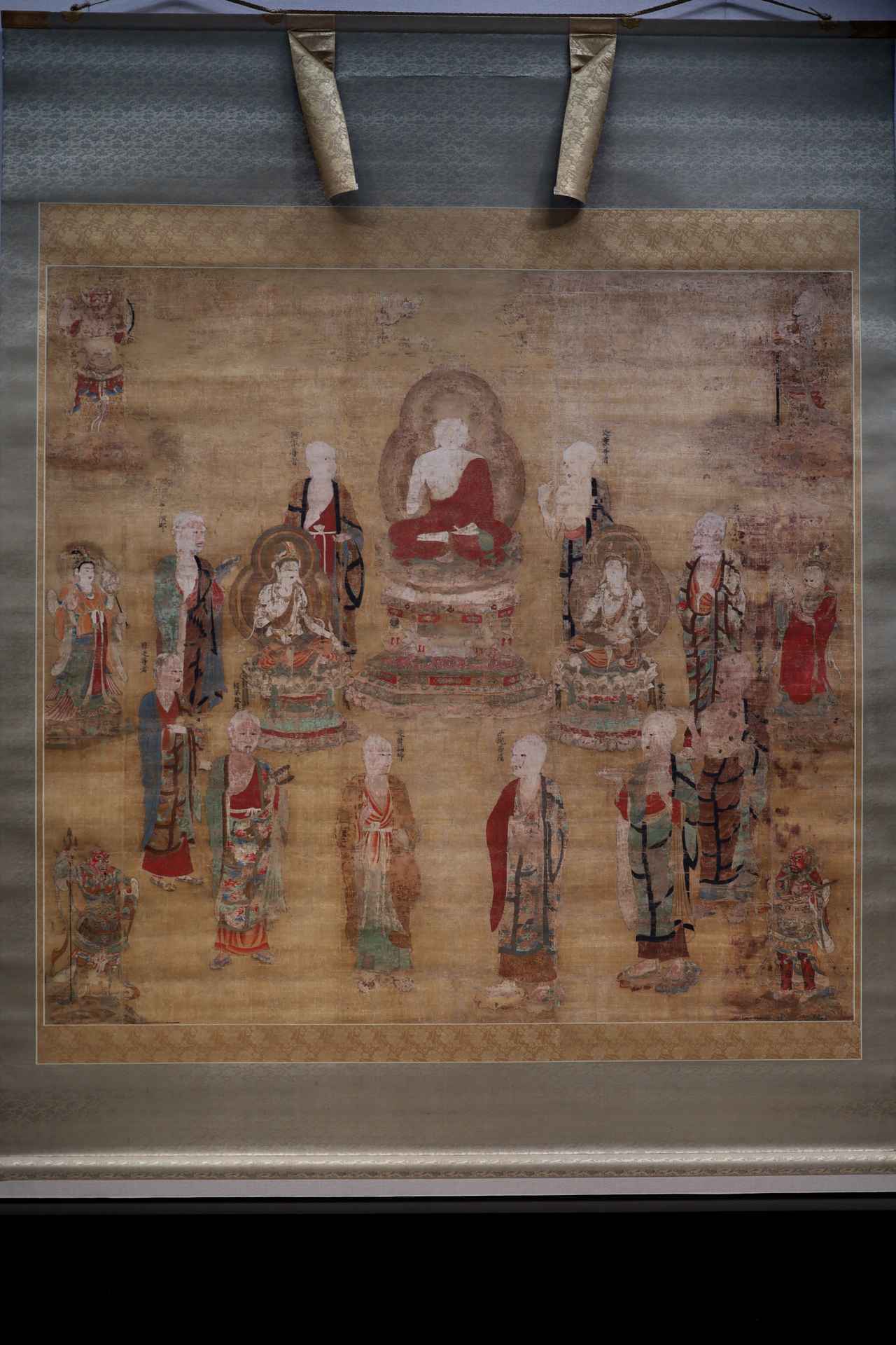 画像: 国宝 具舎曼荼羅 平安時代・12世紀 奈良・東大寺 展示期間：4月19日～5月18日 左足を上に結跏趺坐を組んだ釈迦如来、左右に文殊菩薩と普賢菩薩を十大弟子が取り囲み、その左右に帝釈天・梵天、四方を四天王が固める図像。良質な顔料を用いたとみえ褪色はあまりないが、一部に剥落が激しいのは否めない。なお釈迦の左足が上になった足の組み方はのちのち重要になるので覚えておいて頂きたい。