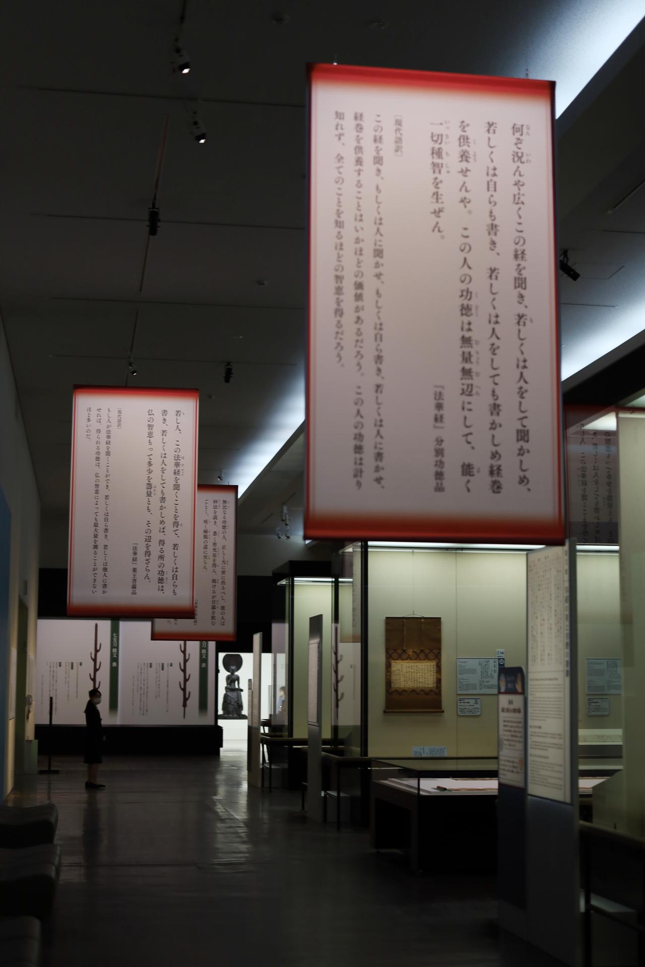 画像: 最後の光の部屋に向かう展示スペースには、天井から法華経、弥勒大成仏経の抜粋と現代語の意訳を記した幕が下げられている