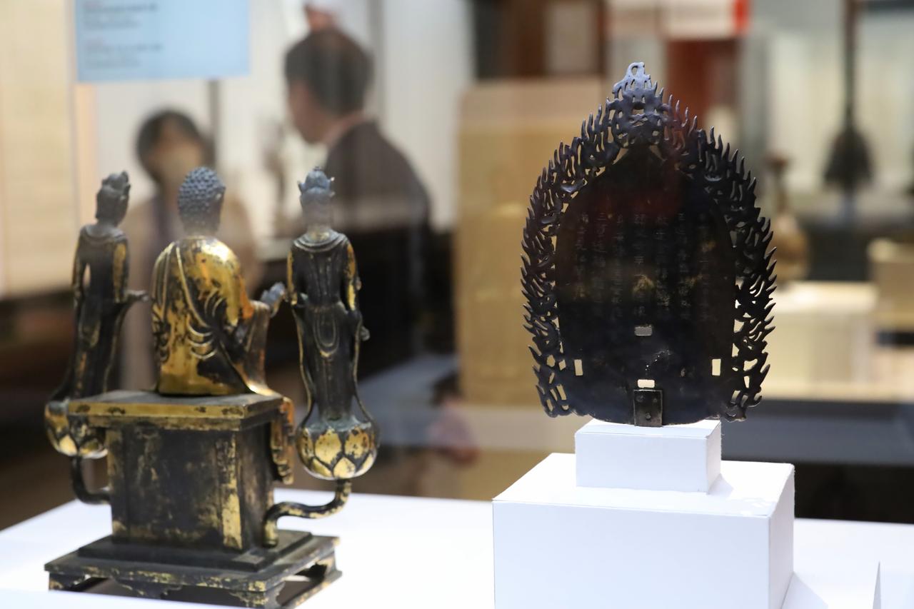 画像: 左）重要文化財 阿弥陀如来倚像および両脇侍立像 飛鳥時代・7世紀 東京国立博物館（法隆寺献納宝物） 右）重要文化財 光背 朝鮮半島・三国時代または飛鳥時代（594年） 東京国立博物館（法隆寺献納宝物） 右の光背の銘文には甲寅という干支が書かれていて製作年代が分かる。本来は釈迦如来の光背だが、明治8年の第一次奈良博覧会では左の阿弥陀如来像の光背に転用されて展示されていた。