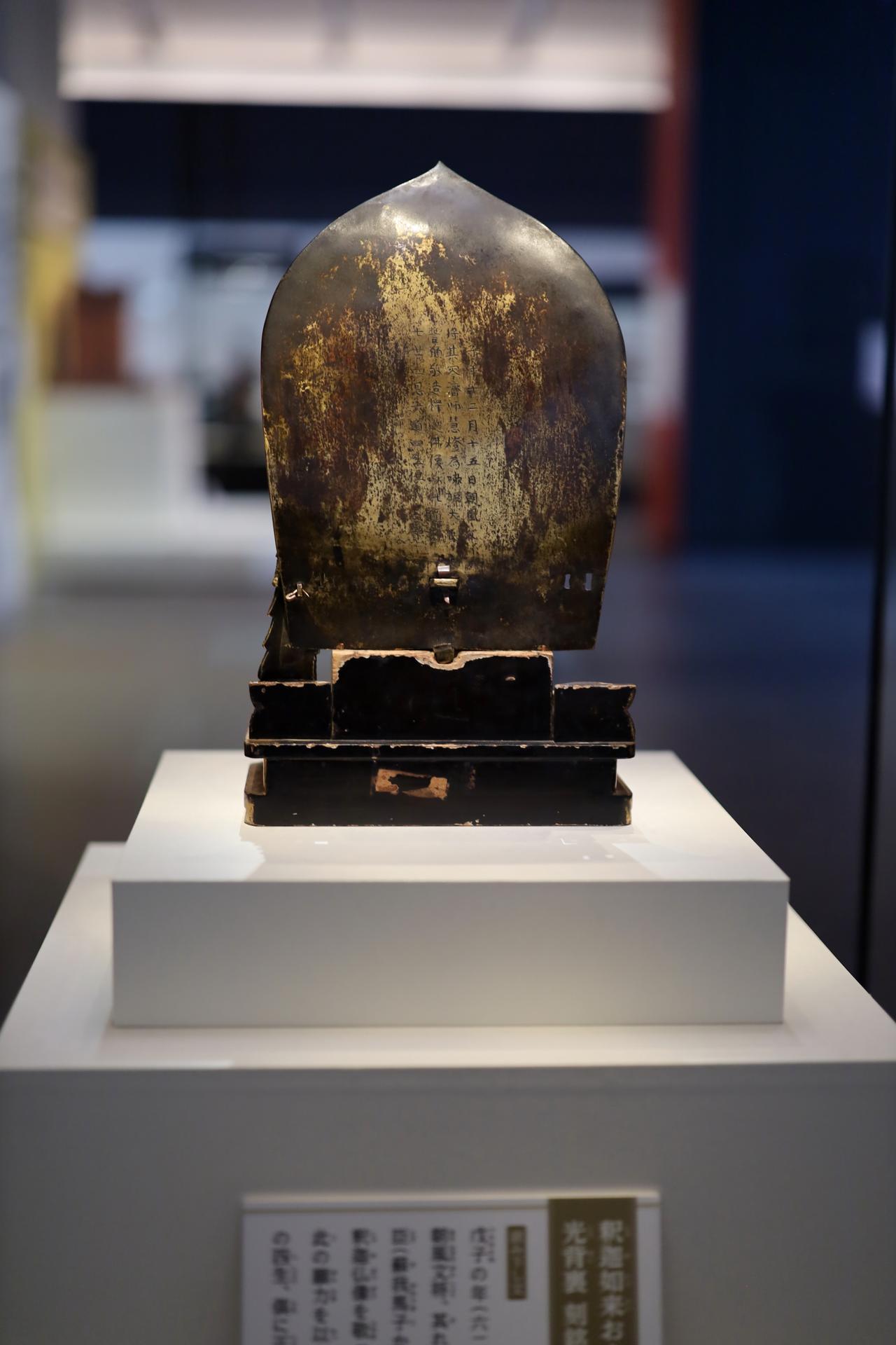 画像: 重要文化財 釈迦如来および脇侍像 飛鳥時代・推古天皇36年（628） 奈良・法隆寺 光背の背面の銘文。下には現代語の意訳の展示パネル