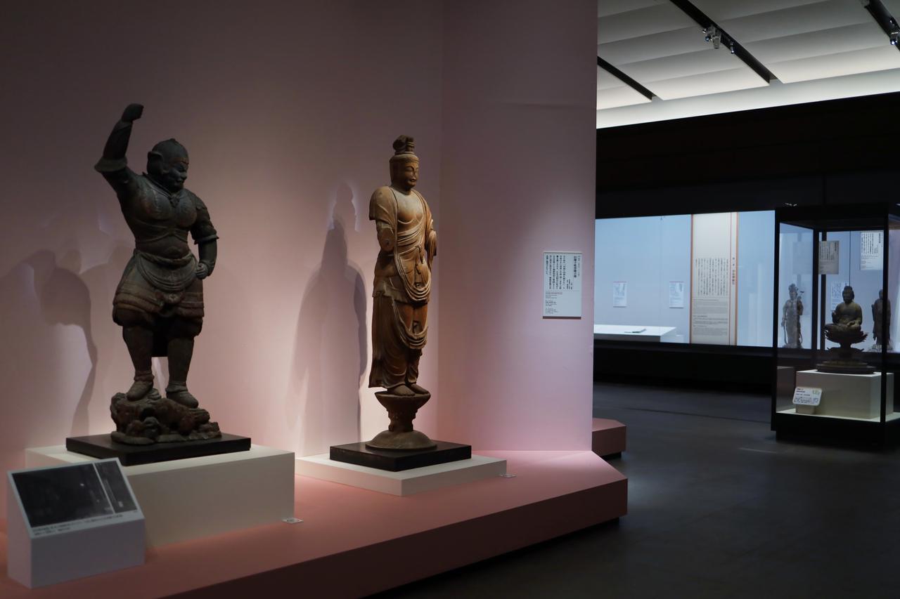 画像: 奈良時代から鎌倉時代まで多様な時代の仏像が並ぶ展示風景。いずれもかつて奈良博に預けられ展示されたか、今も奈良博に寄託されている仏像の名品が揃う。 左から、伝多聞天立像（重要文化財、奈良時代、大安寺）、伝獅子吼菩薩立像（国宝、奈良時代、唐招提寺）、弥勒菩薩立像（鎌倉時代、奈良市林小路町自治会）、薬師如来坐像（国宝、平安時代、奈良国立博物館）、地蔵菩薩立像（重要文化財、鎌倉時代、東大寺）