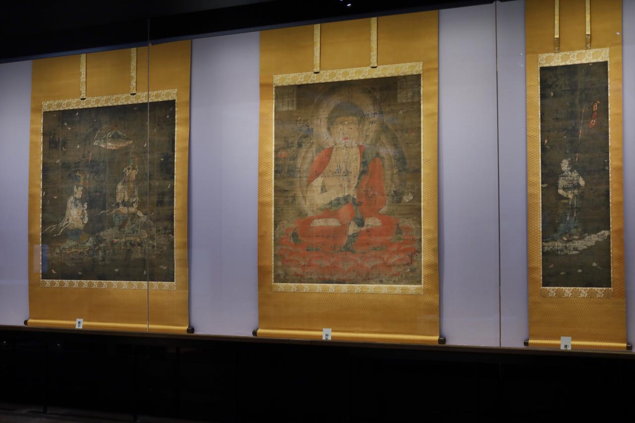 画像: 国宝 阿弥陀三尊および童子像 平安時代〜鎌倉時代・12〜13世紀 奈良・法華寺 展示期間 5月20日〜6月15日 赤い衣で手は説法印を結ぶ阿弥陀如来は、西方極楽浄土に生まれ変わった者たちに教えを説く姿。左幅には死者の魂を運ぶ蓮台を持った観音菩薩と、その上に天蓋を差し掛ける勢至菩薩。右幅は赤い幡を奉ずる童子。奈良時代の図像構成が残った珍しい作例