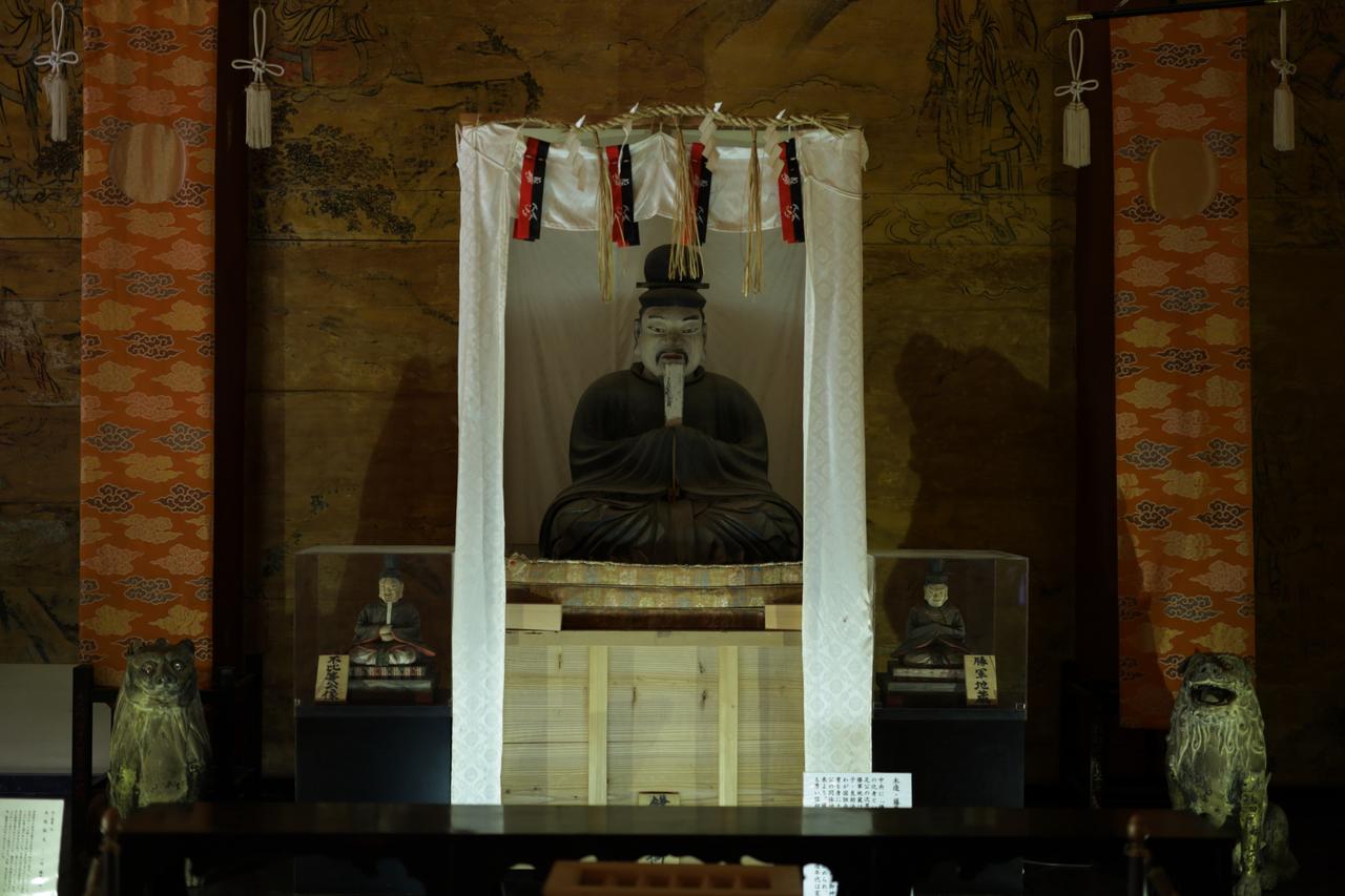 画像: 談山神社の藤原鎌足坐像。三尊形式の脇侍の小像は左が衣冠束帯の不比等像と、右は僧形の定恵ではなく衣冠束帯の勝軍地蔵だが、今回修理された藤原鎌足像のような大織冠尊像や多武峰曼荼羅と基本的に共通する構成。かつては現在の本殿に本尊で本地仏の説法印阿弥陀三尊像と共に安置されていたはずだが、神仏分離令・廃仏毀釈に伴い神廟拝所 (旧・講堂、江戸時代再建・重要文化財)に安置。なお阿弥陀三尊像は同じ奈良県桜井市の安倍文殊院に移され、釈迦三尊として祀られている。