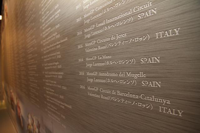 画像: レーサー展示コーナーの背面ボードには、ヤマハがGPで果たしてきた全勝利の記録が記されている。2016年9月3日時点で496勝、通算500勝に向けえて空けてあるスペースは、今季中にも埋まる可能性大。
