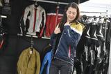画像: この日、レーシングスーツのレンタルや、持ち込みレーシングスーツの補修、新製品の紹介などで大忙しだったクシタニ・ブース。春夏物のジャケットを試着することもできたので、気に入った商品をとりあえず試着中の朱香。「アウトドアっぽくて、イイですよねぇ」とのこと。