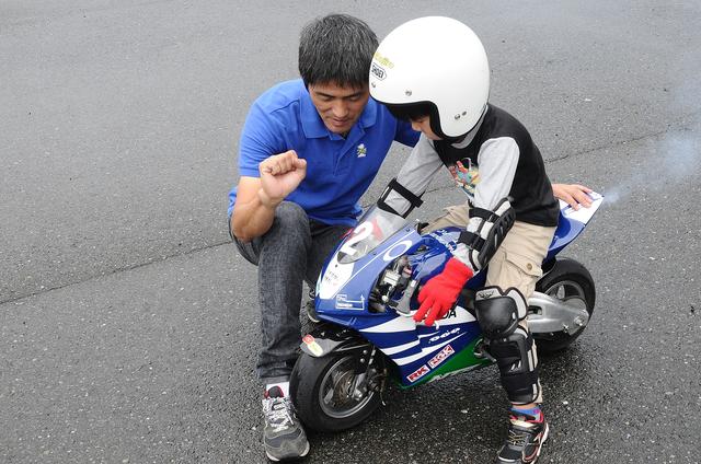 画像: ライダー誕生の瞬間! ゆうたくん、初走行目前! アクセル開ける練習で、村上さんは74が飛び出さないように、足でフロントタイヤを抑えてくれています
