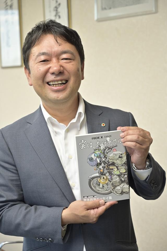 画像: 八戸ノ里ドライビングスクール・代表取締役社長の谷岡 樹校長。東本昌平先生のファンであり、今回の壁画企画の発案者でもある。東本作品の中でも最もお気に入りなのが、谷岡社長が手にするRIDEの巻末エッセイを一冊にまとめた東本昌平エッセイ集「雲は おぼえてル」とのこと。