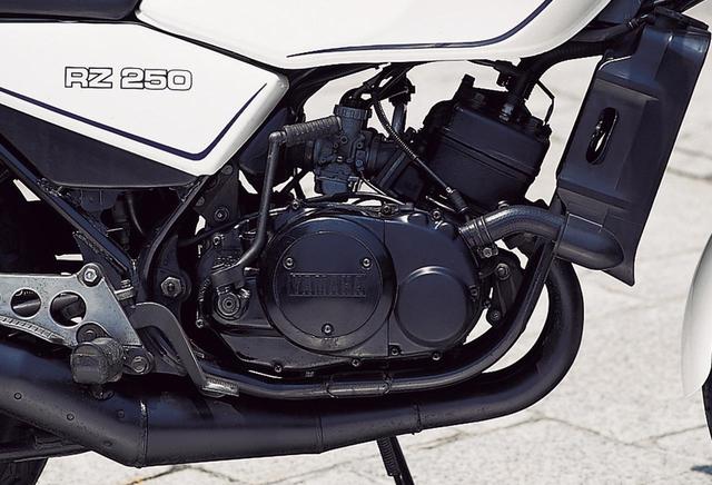 画像: 冷却フィンを持たないTZ250直系のピストンリードバルブ並列2気筒は、ヤマハ量産市販車では初の水冷方式を採用。クランクケースや掃気ポートのレイアウトなどはTZ250と共通とされる。キャブレターはφ26㎜の2連装で、左右インテークマニホールドに両者を接続するバランスパイプが置かれ、中回転域における吸気脈動を促進させることでトルクレンジを拡大、高回転域へのシャープなつながりを持たせている。