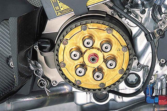画像: 窒化チタンコーティングされた金色のプレッシャープレートが目立つクラッチ。その奥のミッション室カバーは、マグネシウムの削り出しにカニゼンメッキ(無電解ニッケルメッキ)を施したものである。アルミ削り出しパーツの増加で、YZR500と比べてマグネシウムパーツの数は少なくなっている。エンジンオイルの点検窓は、クランクケース側とオイルパン側に1個ずつあり、両者の中間(上にオイルが見えず、下に空気が見えない)が基準と思われる。