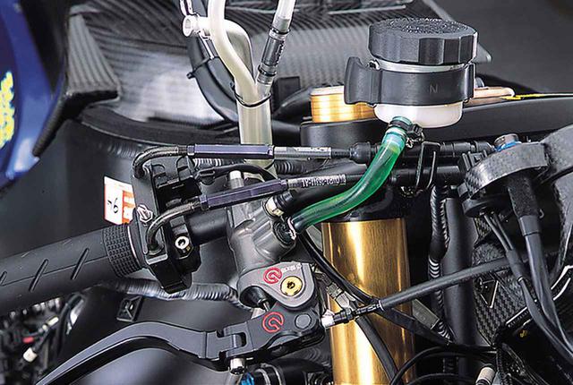 画像: 一般的な大きさのブレーキマスターのリザーバータンクは市販車用パーツの流用と思われる。その真下に、スロットルワイアのジョイントがあり、この部分でワイアの解放/連結ができる。スロットルワイアだけでなく、フロントブレーキホースとクラッチレリーズホースも、途中に設けたイギリスのグッドリッヂ製とおぼしきクイックコネクターによって解放/連結を可能にしている。全体に、セクションごとのメインテナンスはそれぞれの専門メーカーまたはエキスパートに任せ、現場での作業はできるだけ減らそうという設計思想が感じられる。