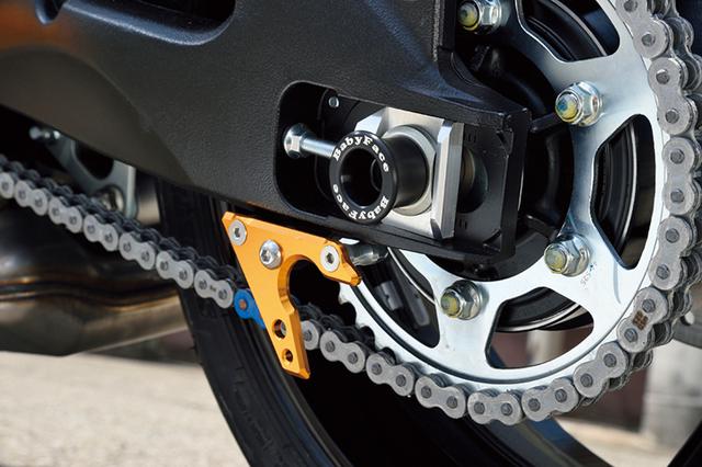 画像: 万一の転倒時にアクスルシャフト両端を保護する「SUZUKI KATANA(19-)アクスルプロテクター」(上写真。6500円+税)と、「リヤアクスルプロテクター」(下写真中央。5000円+税)。スイングアーム下のV字状パーツは「スイングアームスタンドフック」(1万円+税)。上側には本文の「チェーンフック」(3800円+税。本文内写真参照)も装着している。