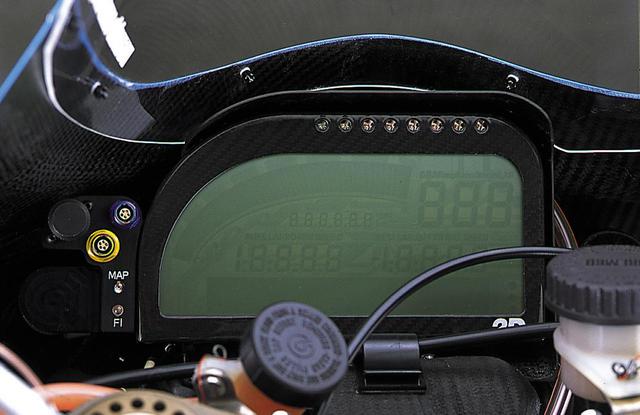 画像: ホンダ以外の4メーカーが使用する2Dのメーターには、左上のRに沿ったバーグラフ式タコメーターの他、大小合わせて4組の数字が並んでいるが、どこにどんなデータを表示させるかは設定次第。メーター枠の上縁に並んだ8個のフラッシュ(おそらく高輝度LED)は、設定した回転数に達すると発光し、シフトアップポイントを知らせる。パネルの左側には、データロガーに記録されたデータの転送やECUのメモリー書き換え時にPCを接続するためのコネクターが並んでいる。