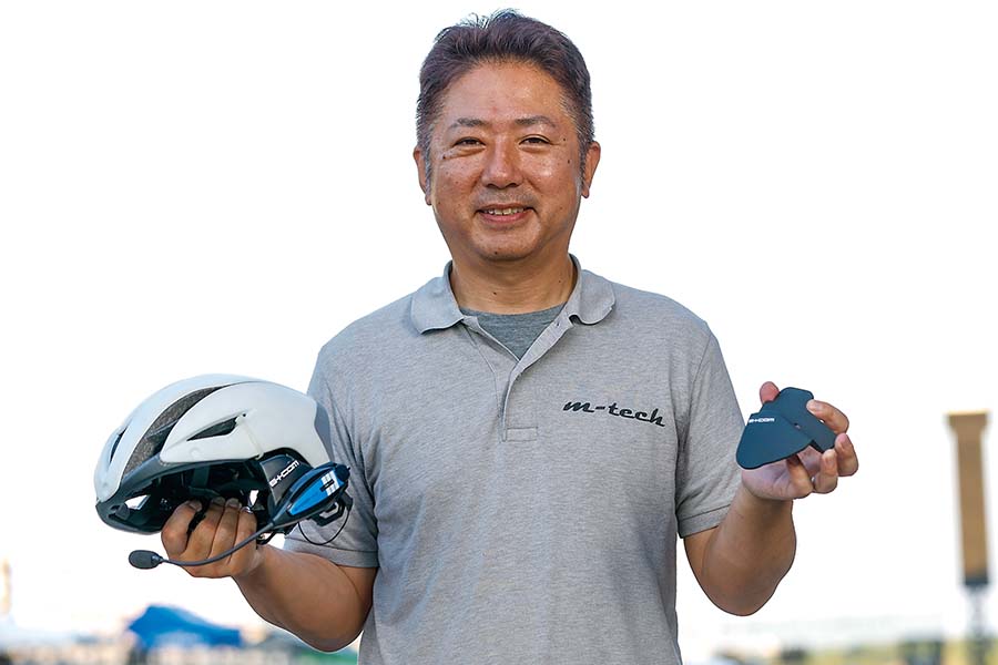 画像: ▲m-tech（エムテック）の松本圭司代表が手に持つのはチームクルーが被るB+COMをセットしたOGK KABUTOのヘルメット（自転車用AERO-R1）と、専用のアタッチメント。そのアタッチメントはm-techの3D LABOで製作したものだ。
