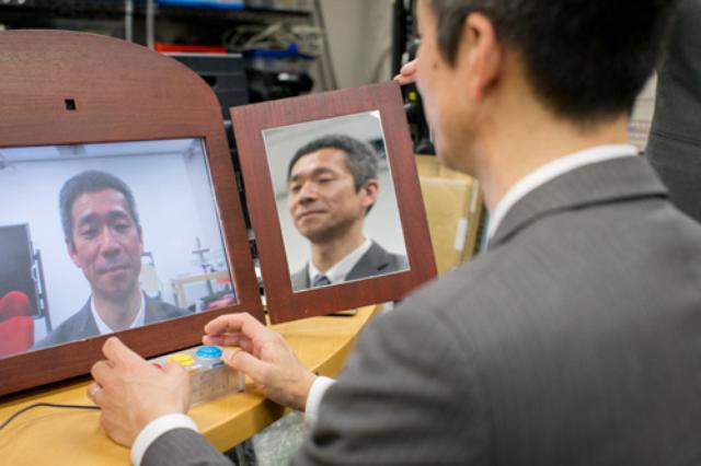 画像: 「扇情的な鏡」の写真 廣瀬研究室の吉田成朗氏が開発した「扇情的な鏡」。普通の表情をしていても、ボタンを押すと微妙に表情が変化する。「悲しいから泣く」のではなく「泣くから悲しい」という感情の揺らぎを実験できる