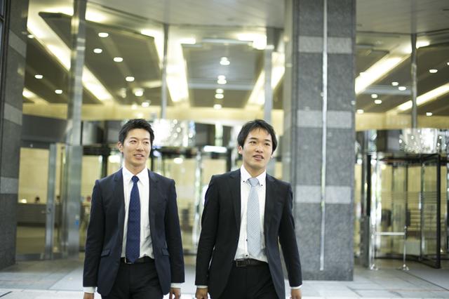 画像: 中堅の営業2人。外出するところを本社エントランスにて撮影。