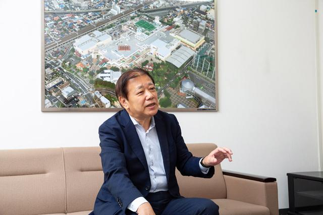 画像: インタビューを受けていただきましたニッケ・タウンパートナーズ株式会社 阪本正一社長。背後の写真は、ニッケコルトンプラザの全体像です。
