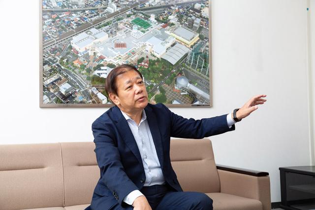 画像: 阪本社長の後ろに飾られているのは、ニッケコルトンプラザ全体の写真です。広大な敷地であることが良く分かります。