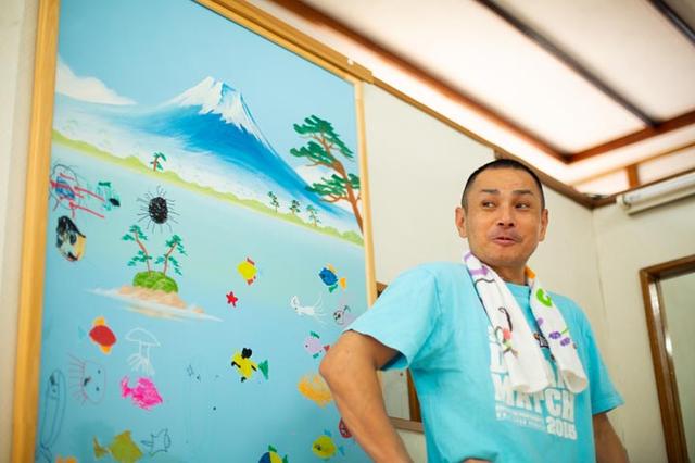画像: 白山湯3代目の白田 敏博さん 。脱衣所には、ラジオ局のイベントで絵師が描いた富士山と子どもたちが描いた絵が飾ってある