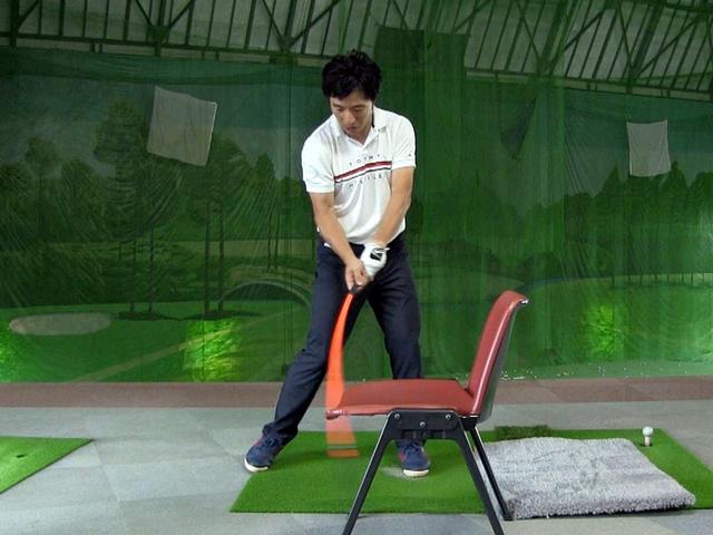 画像: 素振り練習用シャフトと椅子を用いた、しなり戻りの感覚をつかむドリル。しっかりしなりを使えていれば、椅子に引っかかることなく先端部が座面の下に入る