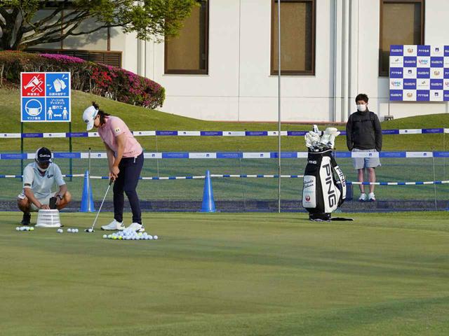 画像: 渋野のパット練習を柵の奥から見守る斎藤トレーナー。現在国内女子ツアーに関しては、トレーナーは有観客試合の場合のみ会場入りができるという(写真は2021年のアクサレディス)