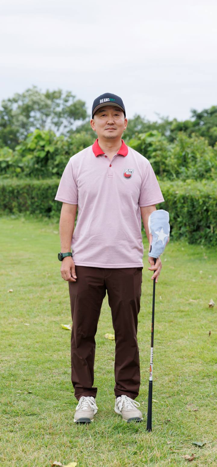 画像: パッと目を引く愛らしいピンクポロにシックなブラウンパンツが生み出す絶妙なトーンバランス。ブラックキャップによってスタイル全体の色合いがグッと引き締まります