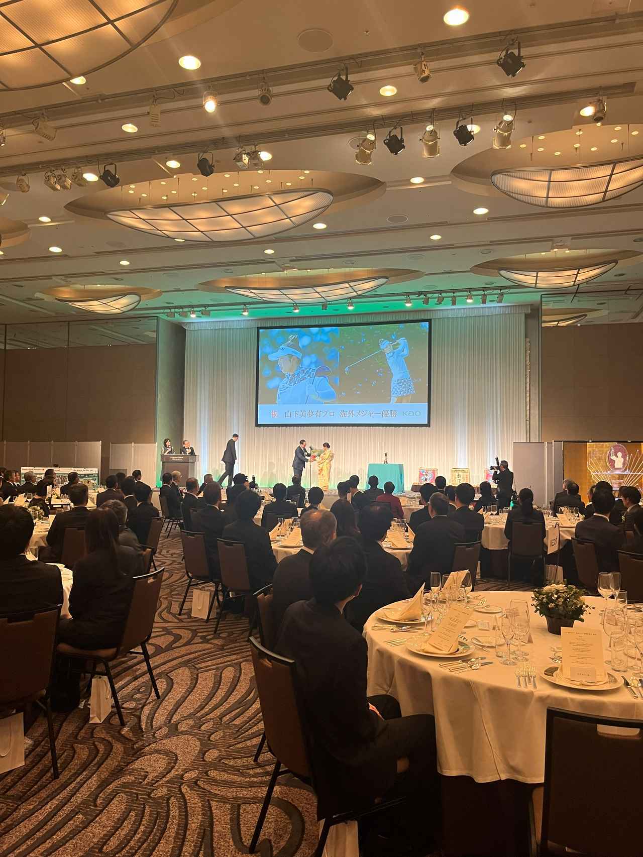 画像: 花王株式会社の社長・長谷部氏より花束が贈呈された。ゲスト席のテーブル番号には、「マジックリン」「メリット」など、花王の商品名が割り当てられていた