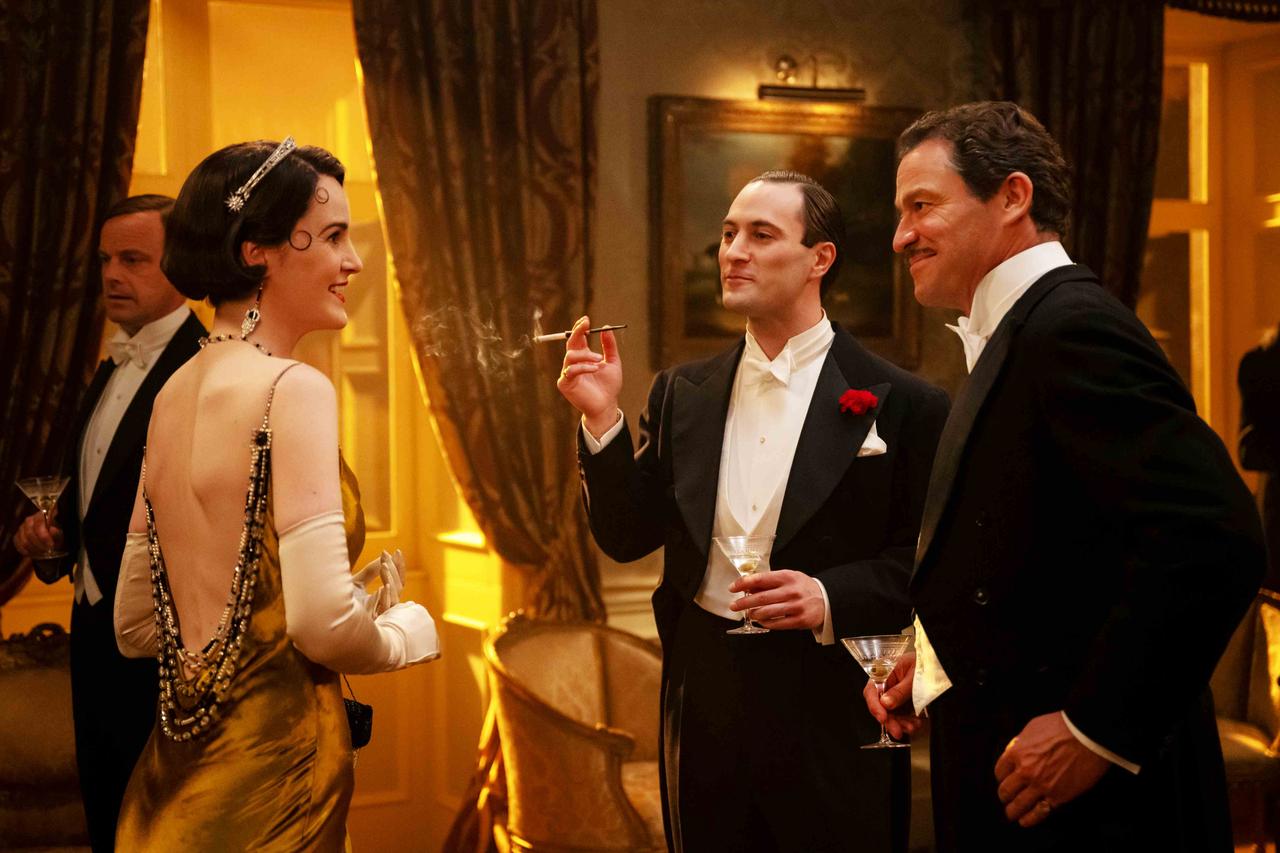 画像: 当時の人気作家、ノエル・カワード（中央）の粋な姿も描かれる。実在のカワードは劇作家・脚本家・俳優・演出家、作詞作曲家など、多彩な才能の持ち主で、デイヴィッド・リーン監督とも組んでいた。 ©2025 FOCUS FEATURES LLC.ALL RIGHTS RESERV