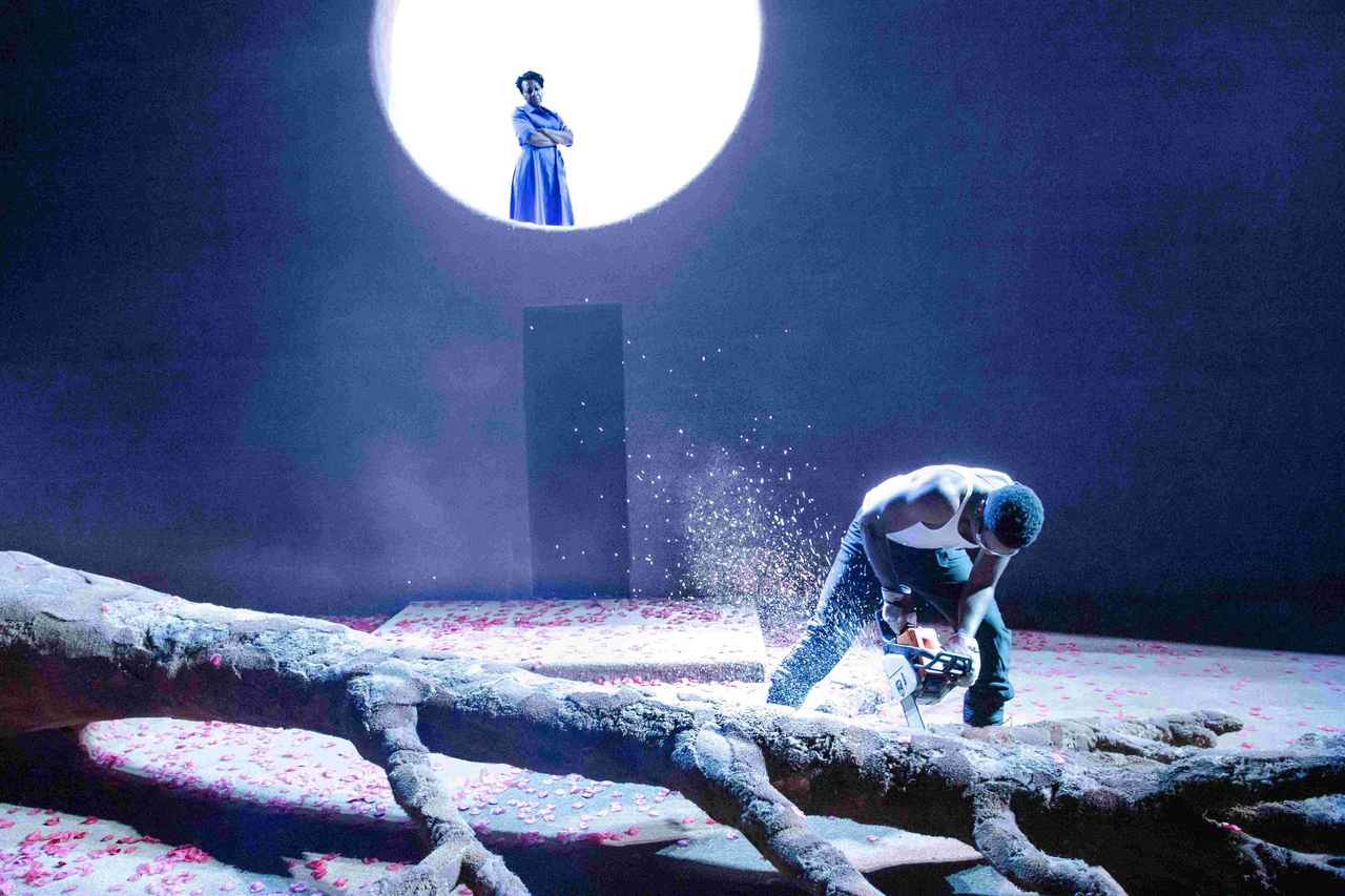 画像: 倒れた大木と後方にある月のような円が舞台の装置として使われ、人物たちの心理を代弁する。 NTLive『みんな我が子』 Photo by Jan Versweyveld