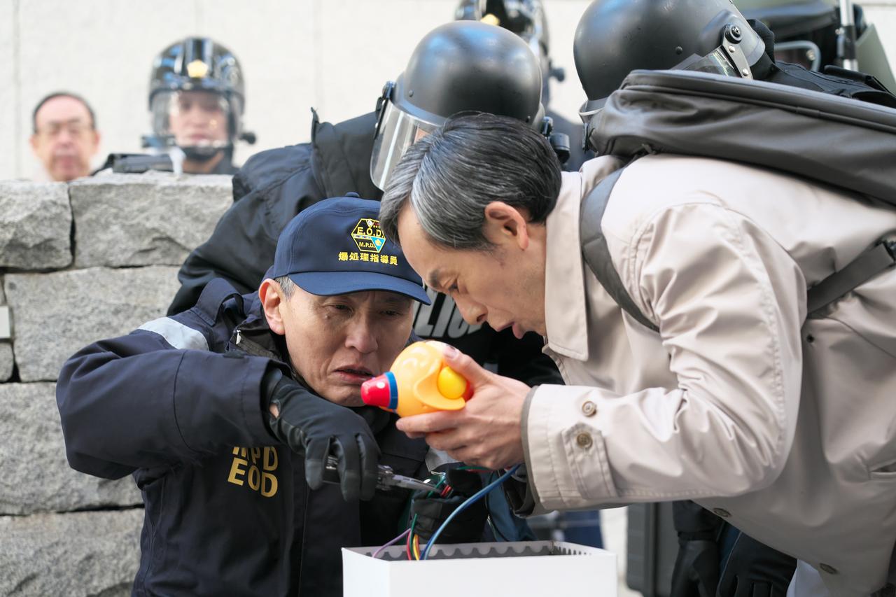 画像: 本作では王明才(滝藤賢一)が爆弾に仕掛けられた湾岸君を手にする