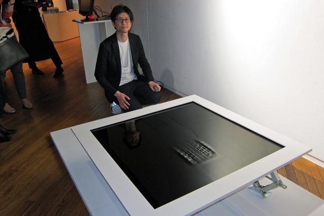 画像: 発表会場に展示された小型の模型と吉泉デザイナー。盤面上に磁性流体技術で浮き出たタイヤのパターンが、クルマがとおりすぎるようなタイヤの軌跡を動いて見せる。