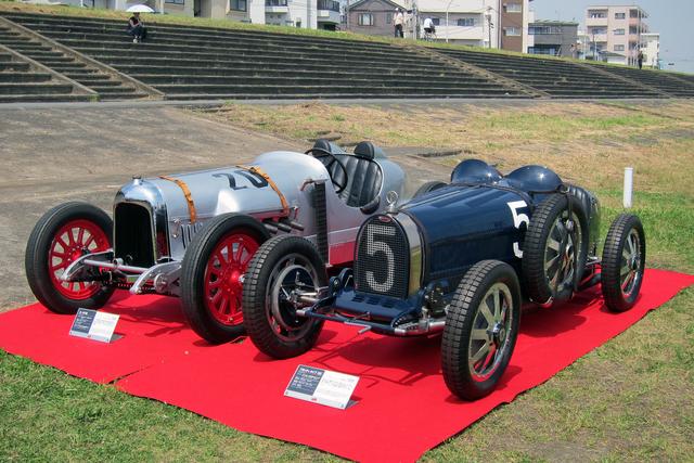 画像: 2016年5月、プレート設置記念式典に展示された、本田宗一郎氏の駆った1924年式カーチス号(左)と1926年式ブガッティT35C。どちらも80年前に出走した実車だ。奥に見えるのがコンクリート製の観客席跡。