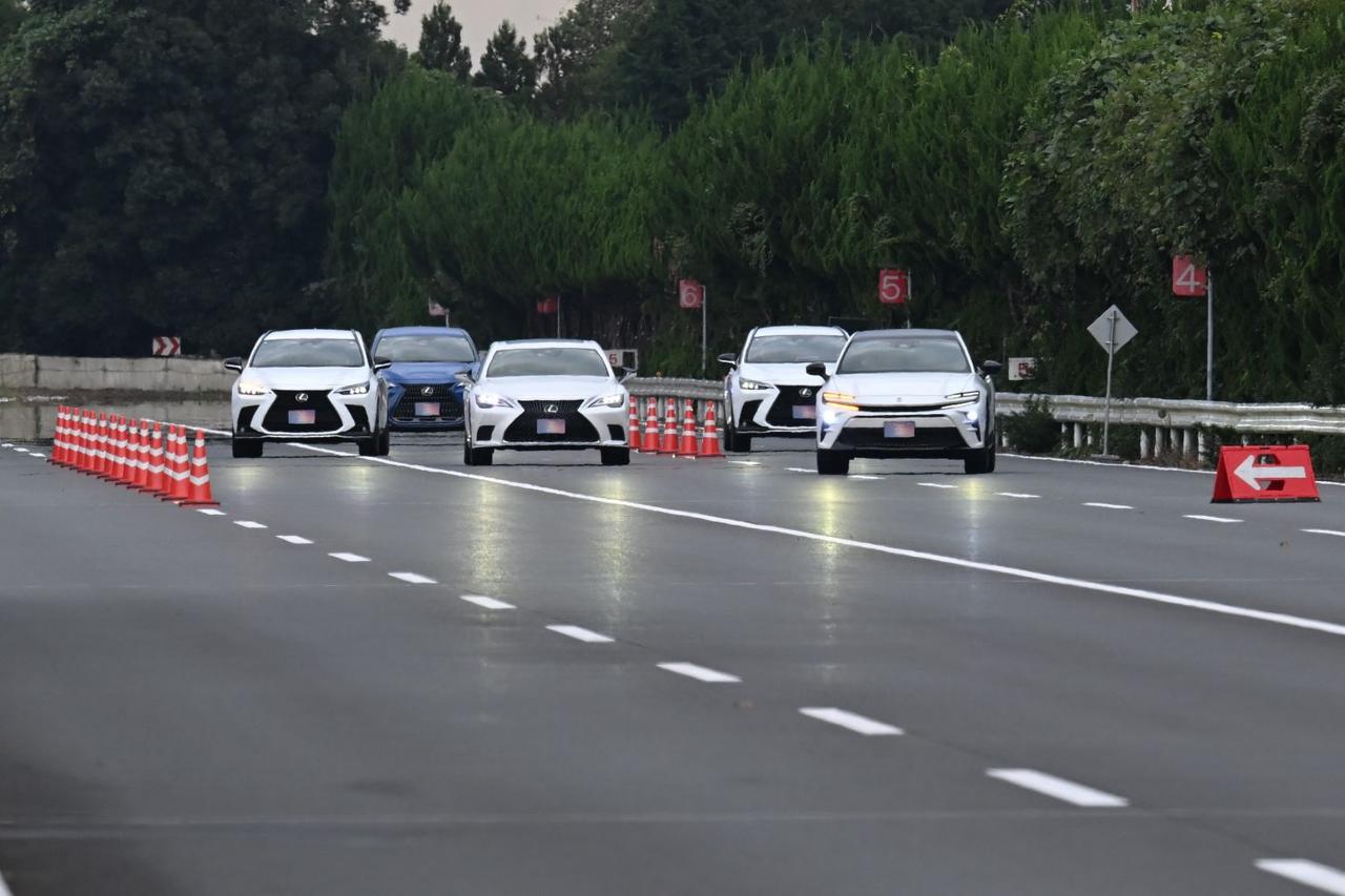 画像: 道路上に置かれたパイロンは「壁」の代わり。つまり車線上のクルマたちからは、左から合流してくる車両は見えていないという設定だ。にもかかわらず写真一番左の車両があらかじめ車線を変更、スムーズな合流のためのスペースを開けている動作は、管制システムが自動制御で行っている。