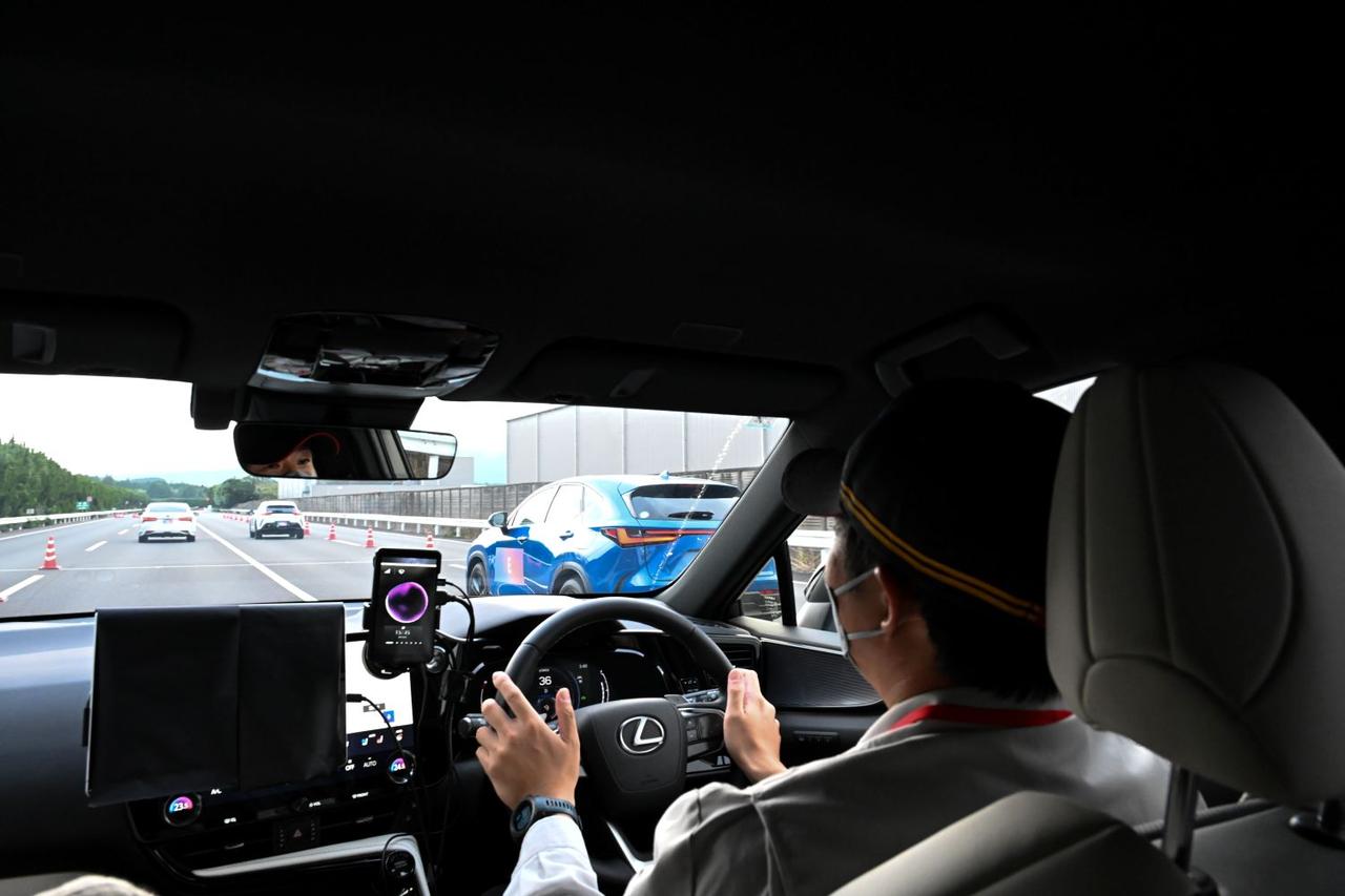 画像: 開発者の運転で、デモンストレーションに参加させてもらうことができた。クルマの台数が多いので、緊張感がしっかり漂う。ちなみにこのクルマは、「合流される」役を担っている。ハンドル左に設置されたスマホに表示されているのが、AIエージェントだ。