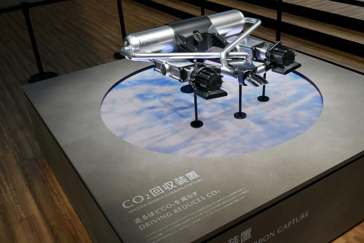 画像: CO2回収装置のプロトタイプ。黒い部分が真空ポンプ、その奥にある四角い箱に吸着剤を塗布したユニットが収められている。中央のパイプから、CO2を除去した排気が外部に排出される。