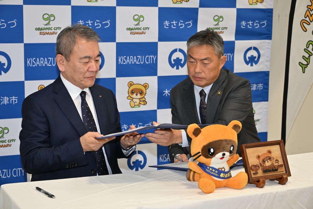 画像: 締結式は木更津市役所内で行われ、七五三木社長（左）と渡辺市長の間で締結文書が交わされた。