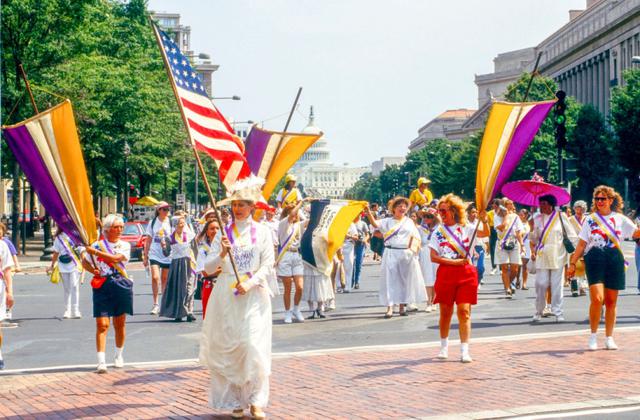 画像: 1995年、性別を理由に市民の投票権を否定することを禁じるアメリカ合衆国憲法修正第19条の制定75周年を記念した行進で全国女性党の旗を翻す参加者たち。ちなみに、イギリスの婦人参政権運動のシンボルカラーは「紫」「白」「緑」の3色。