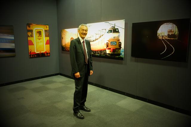 画像: ▲「国鉄カラー」の列車の作品を前にする猪井貴志さん。 cweb.canon.jp