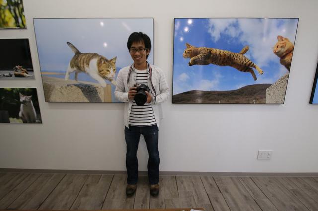 画像: ▲展示作品「飛び猫」を前にする五十嵐健太さん。五十嵐さん猫の写真集「飛び猫」、「フクとまりも」なども同展で購入できる。 k-igarashi.com