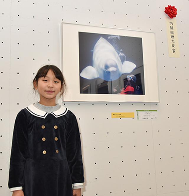 画像: 第21回総合写真展で内閣総理大臣賞を受賞した福岡県在住の小学3年生 下條 良菜さん(9歳) ❇︎学年・年齢は受賞当時のものです。 受賞作品「バブルリング」の前で
